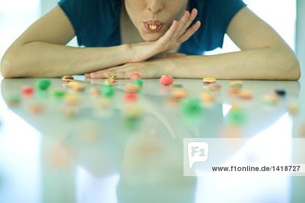 Tischaufstrich mit Süßigkeiten  Frau ruht Kopf auf Armen  hält Süßigkeiten zwischen den Zähnen