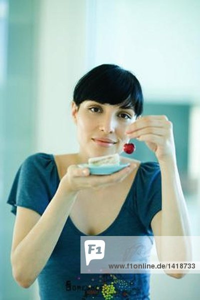 Woman holding up fresh cherry in one hand and saucer with finger sandwiches in the other hand