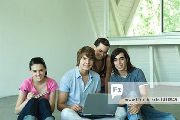 Four teen friends sitting on floor together  using laptop