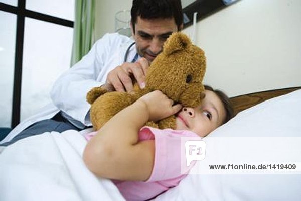 Arzt hält Teddybär bis zum Gesicht des kranken Kindes