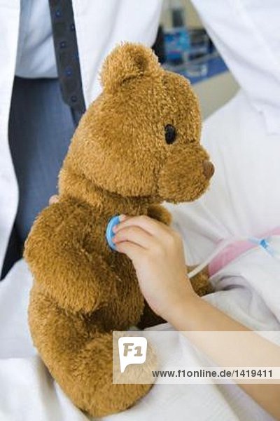 Kind hält Spielzeug-Stethoskop an Teddybär  Teilansicht