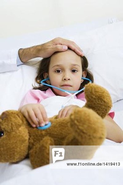 Kind hält Spielzeug-Stethoskop an Teddybär  Arzt spürt die Stirn des Kindes