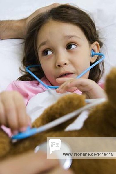Kind hält Spielzeug-Stethoskop zu Teddybär  im Gespräch mit dem Menschen