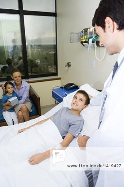 Boy lying in hospital bed surrounded by family and doctor