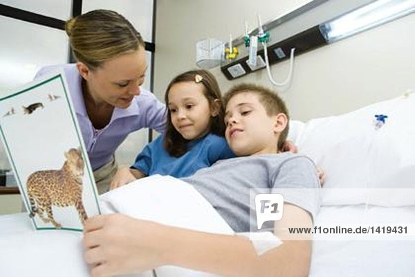 Junge im Krankenhausbett  Lesebuch mit Mutter und Schwester