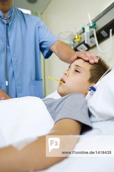 Junge im Krankenhausbett liegend  Arzt bei Fieber und Stirngefühl