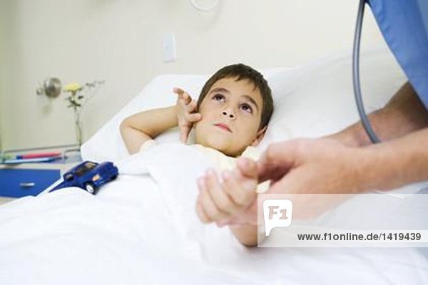 Boy lying in hospital bed  looking up at doctor