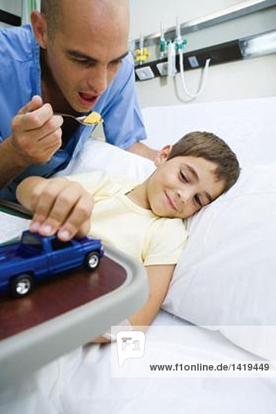 Junge liegt im Krankenhausbett  Arzt ermutigt Junge zum Essen