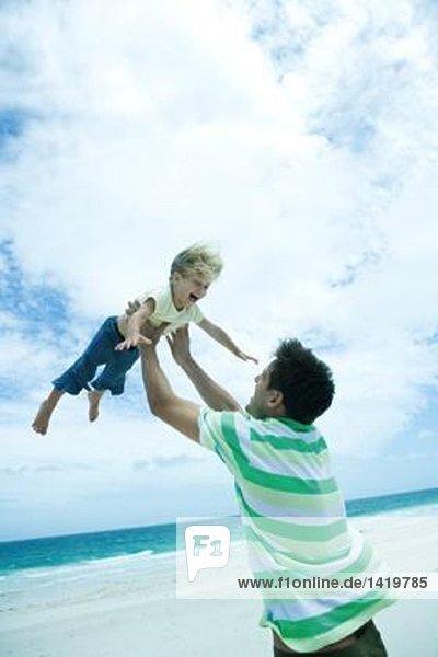 Mann hebt Kind am Strand in die Luft