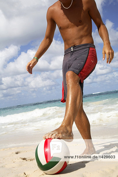 Junger Mann spielt Fußball am Strand