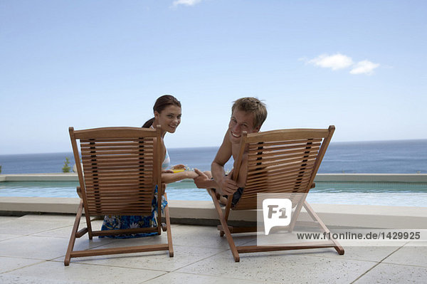 Paar sitzt in Liegestühlen am Swimmingpool