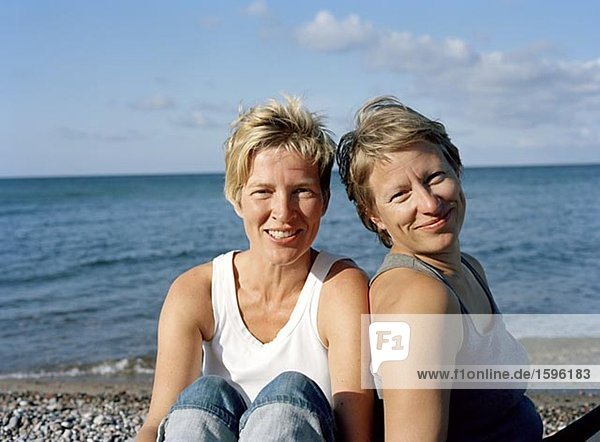 Porträt von zwei Frauen sitzen an einem Strand.