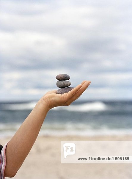 A hand holding up stones with the ocean in the background.