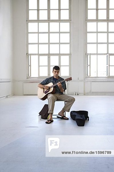 Ein Mann sitzt in eine helle und luftige Zimmer Gitarre zu spielen.