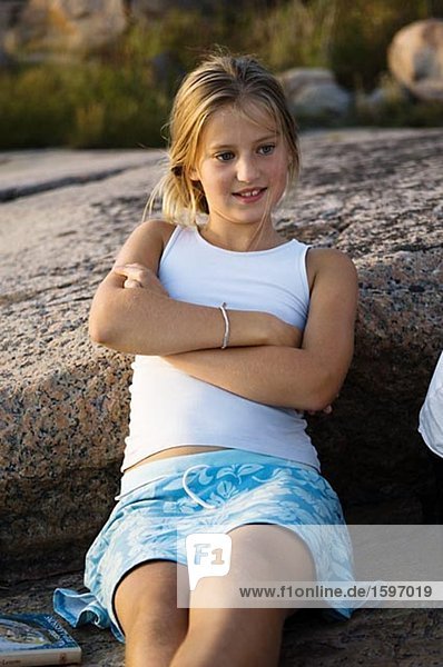 Ein Mädchen sitzend auf einem Felsen am Meer.