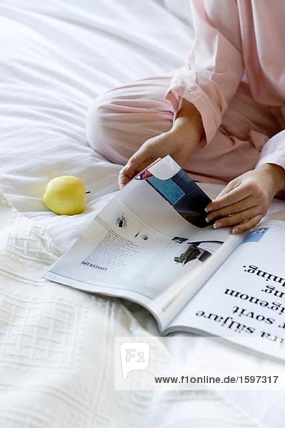 Eine Frau sitzen in einem Bett lesen eine Zeitung.