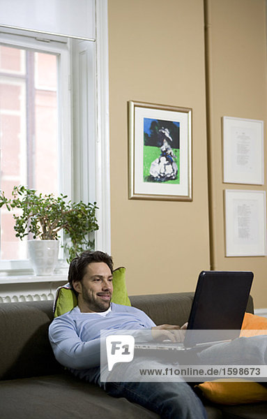 Ein Mann mit einem Computer in einem Sofa sitzen.
