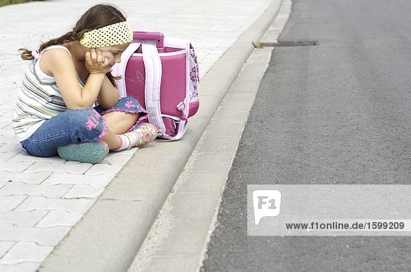 Seitenansicht Mädchen mit Schultasche am Straßenrand sitzen