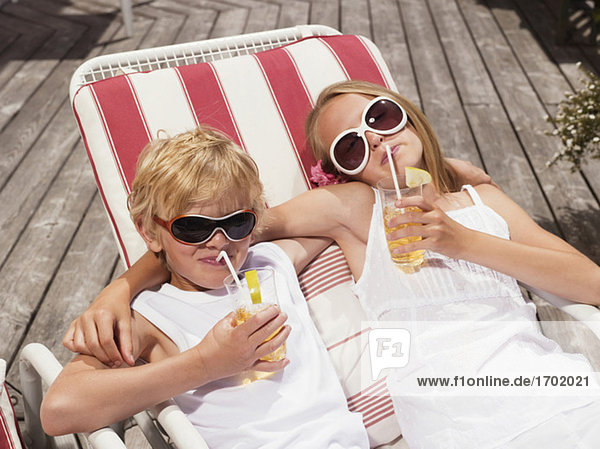 Brother and sister lying in deck chairs  drinking juice
