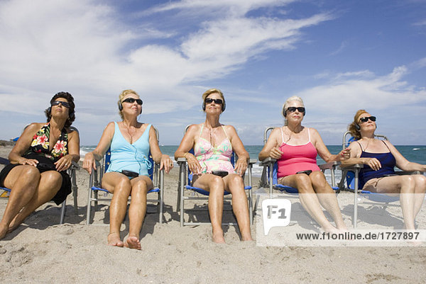 Frauen hören Kopfhörer am Strand