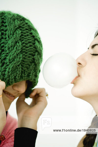 Zwei junge Freundinnen  eine Blasen mit Kaugummi  die andere zieht den Hut über die Augen.