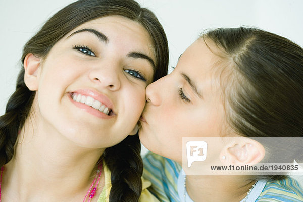 Zwei junge Freundinnen  eine küsst die andere auf die Wange.