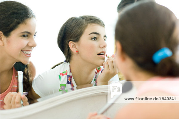 Junge Freundinnen schauen in den Spiegel und schminken sich.