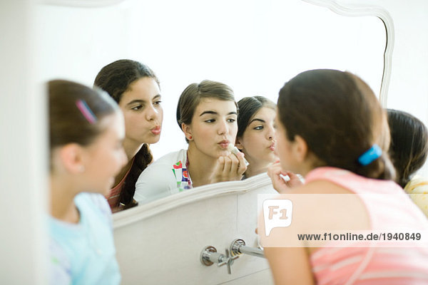 Junge Freundinnen schauen in den Spiegel und schminken sich.