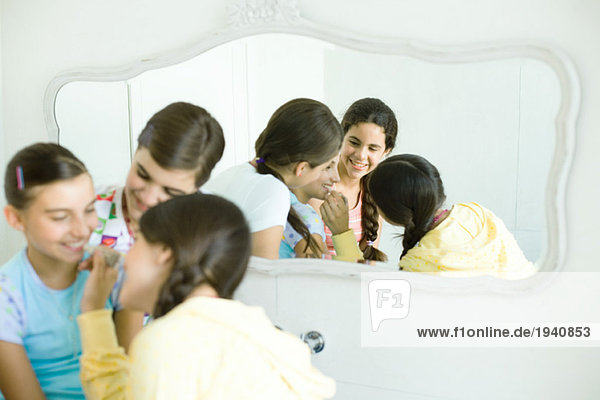 Young female friends putting make-up on younger girl