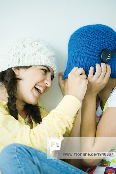 Two young female friends  one hiding face under hat mouth