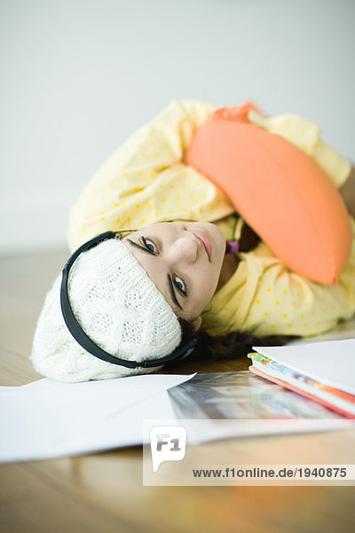 Young woman lying on floor listening to headphones  neglecting homework