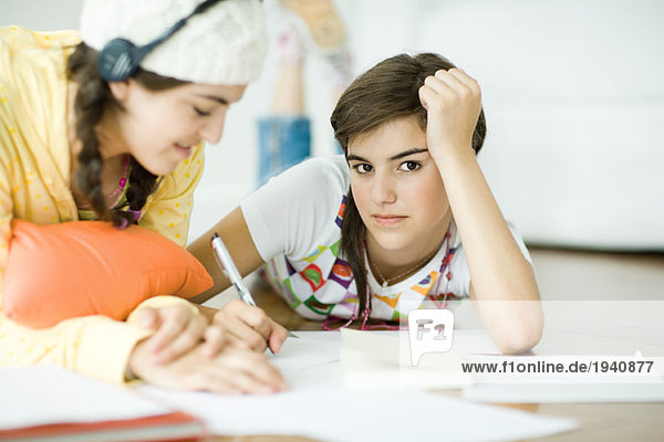 Two young female friends lying on floor  doing homework together