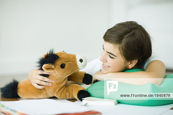 Teen girl lying on floor  smiling at stuffed toy horse