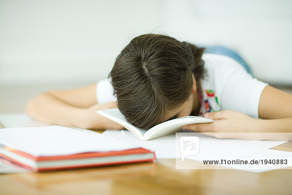 Teenagerin auf dem Boden liegend  Hausaufgaben machend  ruhendes Gesicht im Buch