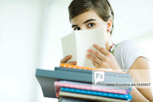 Teen girl with stack of homework  hiding face behind book  portrait