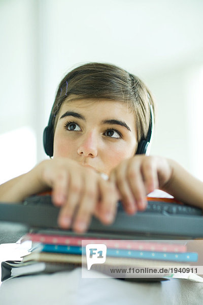 Teen girl with stack of homework  listening to headphones  portrait