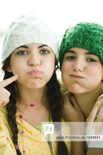 Young female friends wearing knit hats  puffing out cheeks
