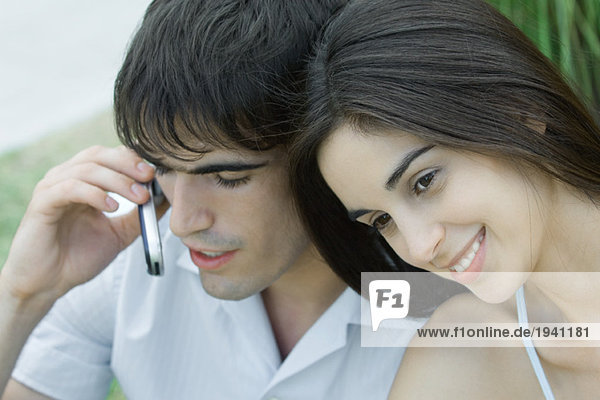 Young couple  woman leaning head against man while man uses cell phone  head and shoulders  portrait