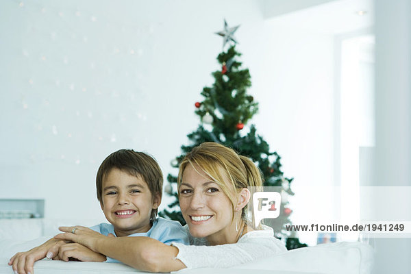 Junge und Mutter auf Sofa  Weihnachtsbaum im Hintergrund  lächelnd vor der Kamera