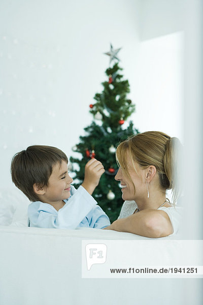 Junge und Mutter auf dem Sofa lächeln sich an  Weihnachtsbaum im Hintergrund