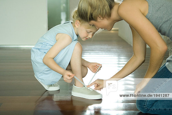 Mutter hilft dem kleinen Mädchen  Schnürsenkel zu binden.