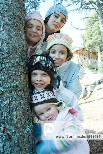 Group of teens and children dressed in winter clothes  posing next to tree  portrait