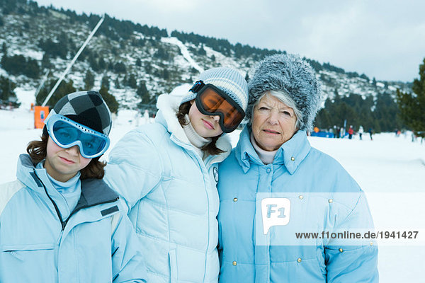 Senior woman with teen and preteen granddaughters  wearing coats and hats  standing in snowy landscape