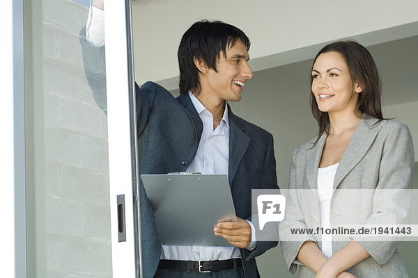 Männlicher Immobilienmakler  der dem weiblichen Kunden das Haus zeigt  steht an einer Glasschiebetür  Frau schaut hinaus  lächelnd