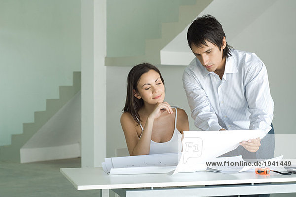 Couple looking at blueprints together  man leaning over table  holding up blueprint