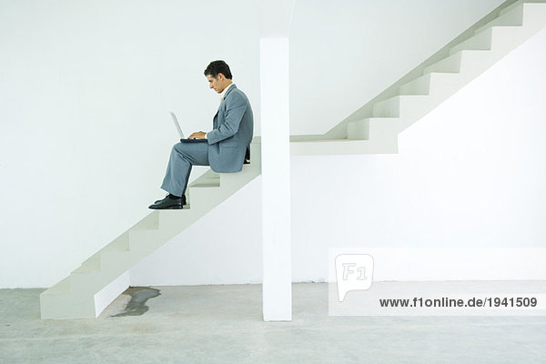 Mann im Anzug auf der Treppe sitzend  mit Laptop