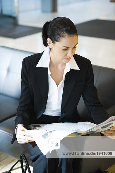 Young businesswoman sitting on couch  reading newspaper