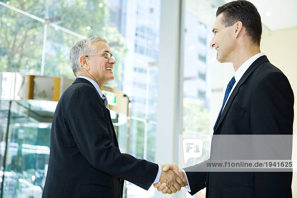 Two businessmen shaking hands  smiling at each other  waist up