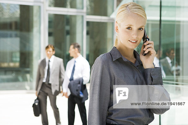 Junge Geschäftsfrau mit Handy  lächelt in die Kamera  Geschäftsleute im Hintergrund