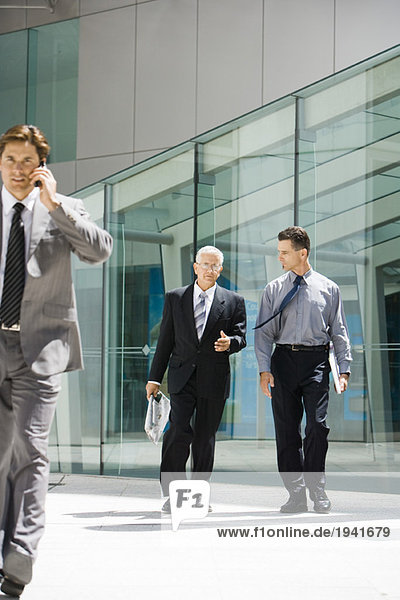 Two businessmen walking in front of building  discussing  one looking at camera